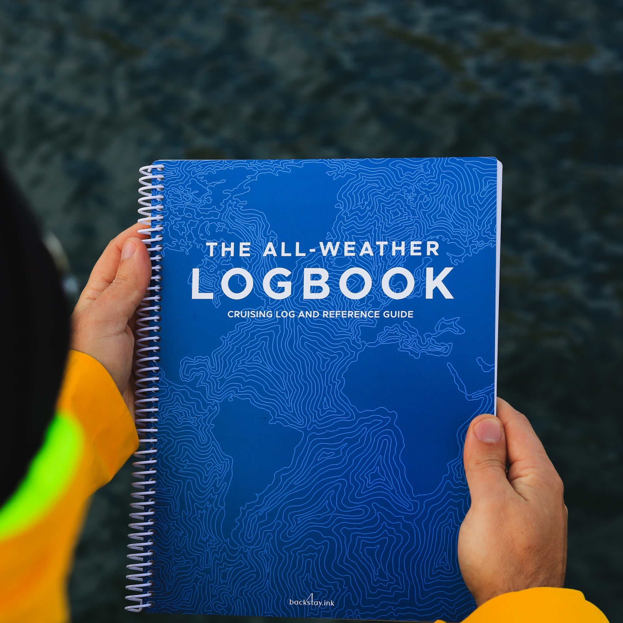 Waterproof all-weather sailing logbook held on deck in rain gear.