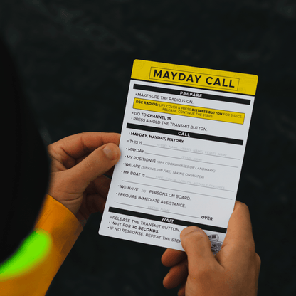 Waterproof Mayday call card with VHF Channel 16 instructions held over water on a boat.